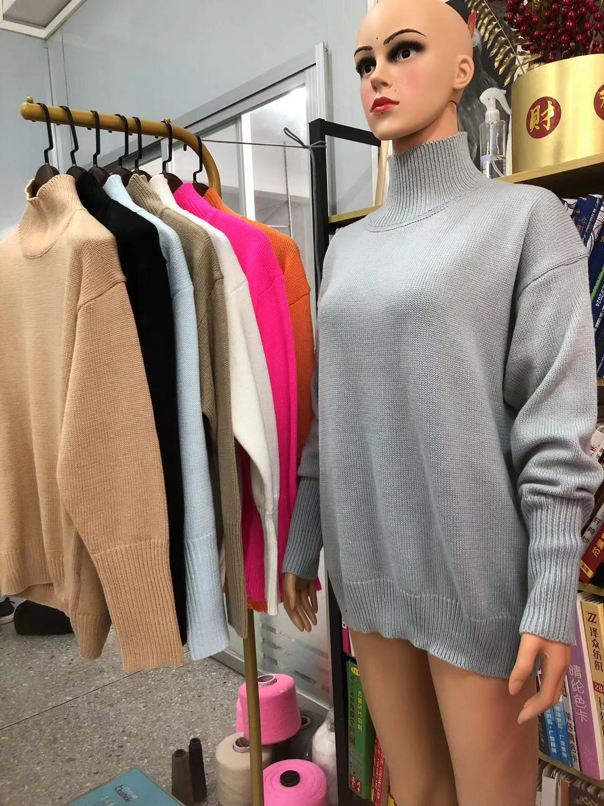 Chandail col montant en tricot gris sur mannequin, avec portant de plusieurs coloris en arrière-plan