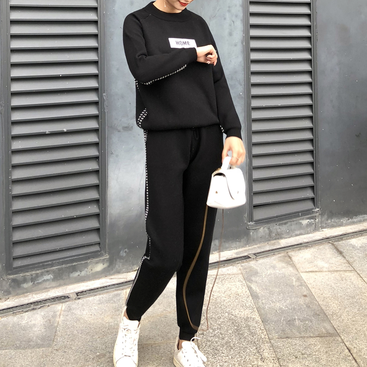 Femme portant l'ensemble en tricot et cachemire noir, sweat-shirt à écusson HOME et pantalon assorti, tenant un sac blanc en extérieur