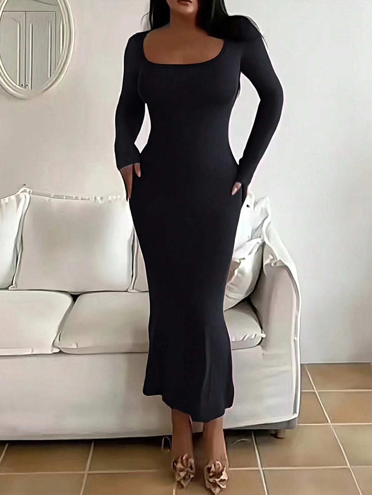 Robe moulante noire à manches longues, portée devant un canapé, vue de face