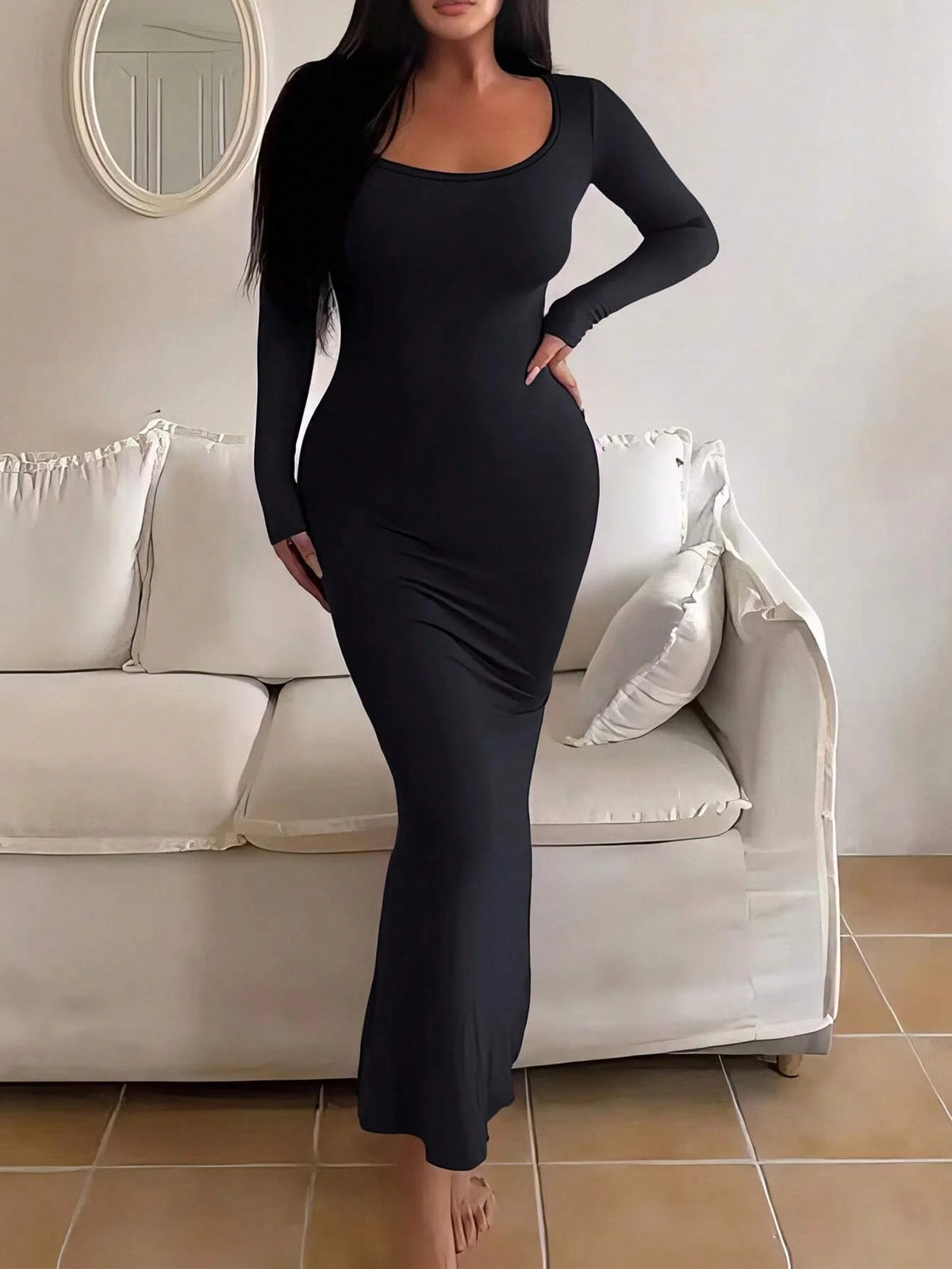 Robe moulante noire à manches longues, portée devant un canapé, vue de trois quarts